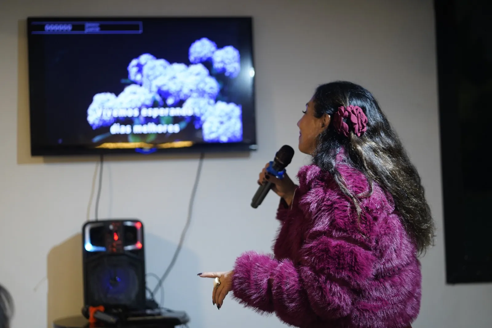 Convidada cantando com o microfone do kit karaokê do Pronto Pra Festa, com a letra na TV e a caixa de som ao lado